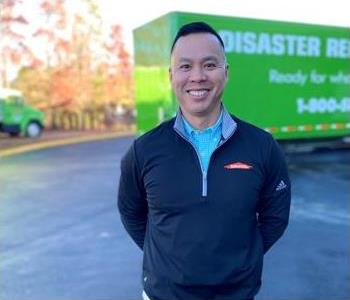 male employee smiling in front of green SERVPRO trucks